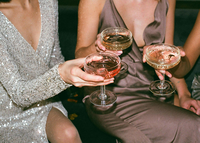 Three people in elegant dresses holding cocktails, illustrating luxury industries and costly lifestyle habits.