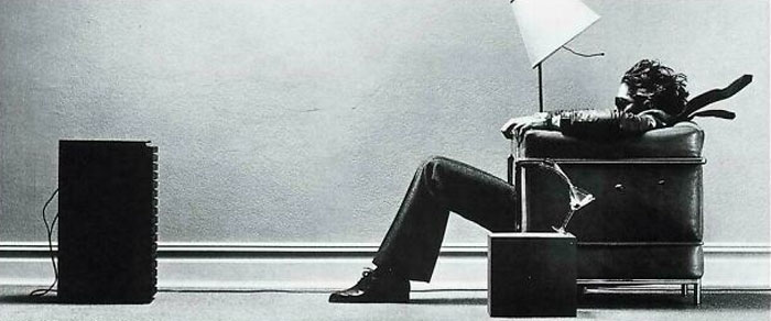 Black and white photo of a man sitting on a chair watching a vintage TV, evoking nostalgia and creaking joints memories.