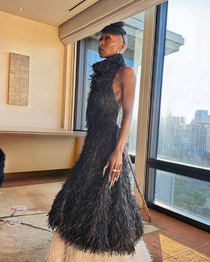 Cynthia Erivo posing indoors wearing a textured black dress, highlighting her oddly large hands in natural light by the window. Cynthia Erivo posing indoors wearing a textured black dress, highlighting her oddly large hands in natural light by the window.