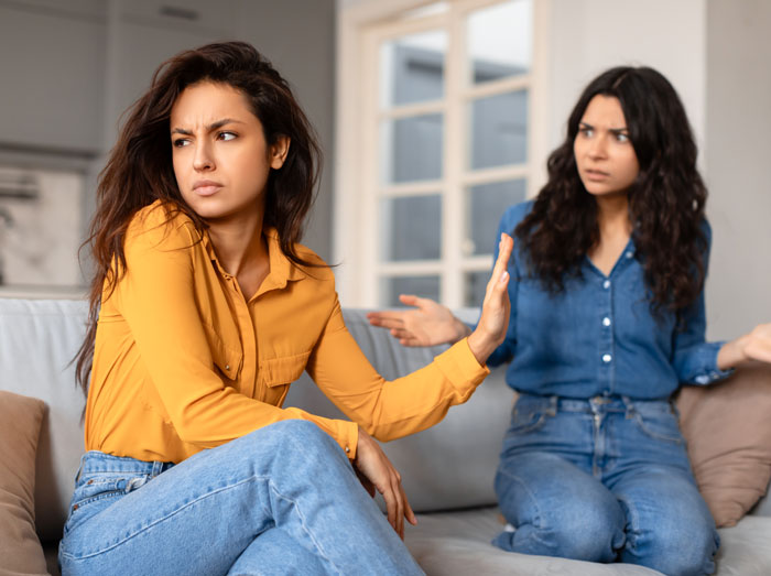 Two women having a tense conversation on a couch, highlighting woman upset over dog and old cat conflict. Two women having a tense conversation on a couch, highlighting woman upset over dog and old cat conflict.
