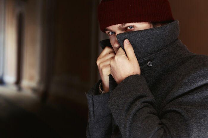 Young man in a gray coat and red beanie hiding face, embodying crazy things people do believing their ex will always pine for them