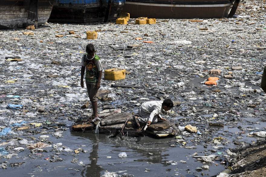 Children navigating a heavily polluted water area filled with trash, highlighting top dirtiest countries and pollution rankings.