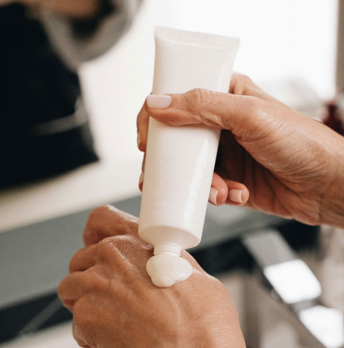 Close-up of a person squeezing lotion from a white tube onto their hand, highlighting skincare routine details.