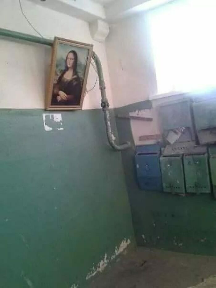 Faded green hallway with old mailboxes and a crooked framed Mona Lisa hanging near exposed pipes, Eastern Europe humor.