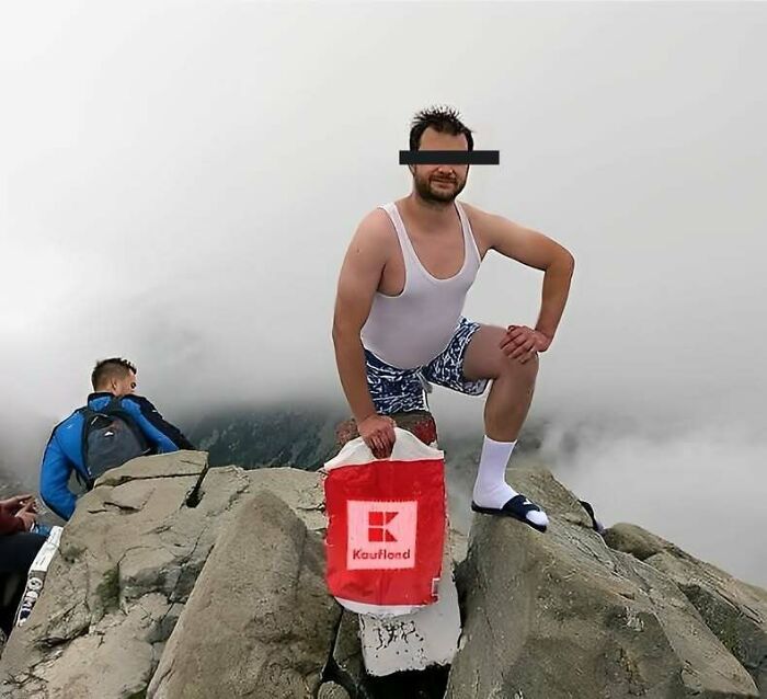 Man in funny outfit posing on rocky mountain peak holding a Kaufland bag, a relatable Eastern Europe meme image.