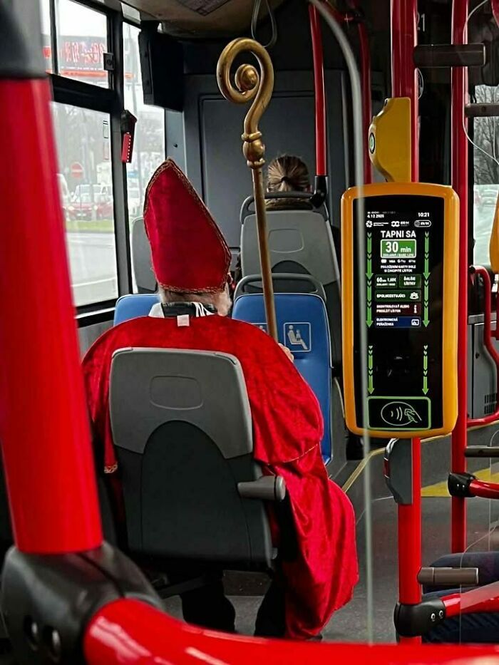 Man dressed in Eastern European bishop costume sitting on a public bus with a staff, capturing a humorous cultural moment.