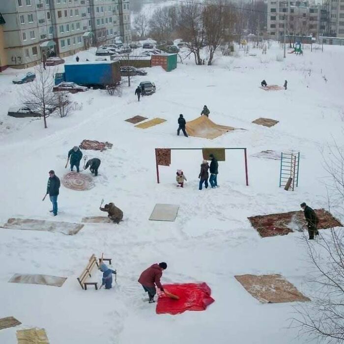 People beating carpets outside a Soviet-era apartment block in winter snow, a nostalgic Eastern Europe scene meme.