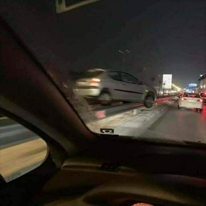 Car seemingly floating above guardrail on a busy road at night, a humorous Eastern Europe meme moment.