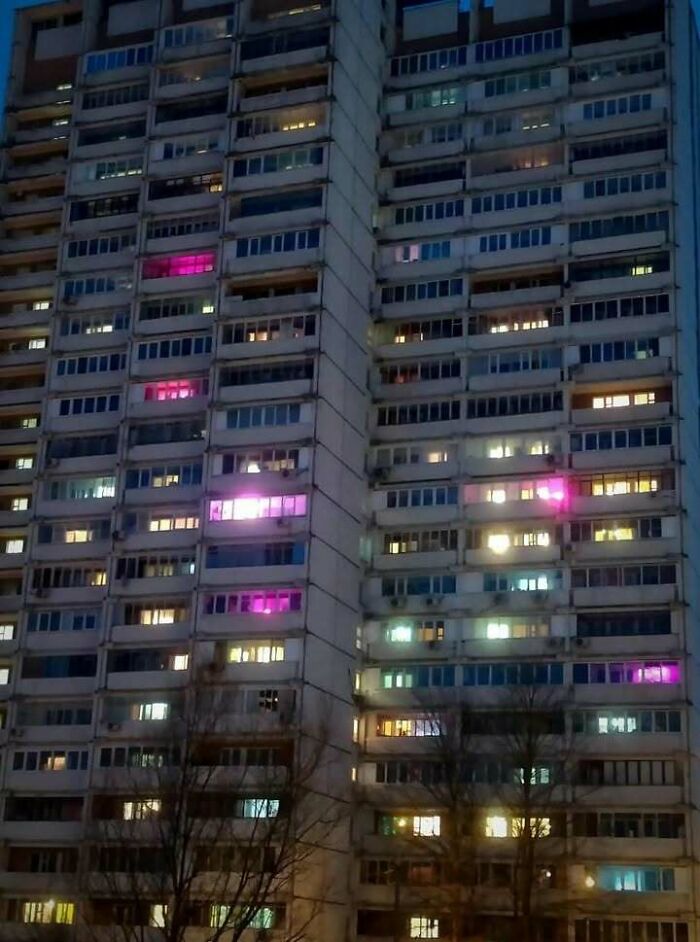Eastern Europe apartment building at night with multiple lit windows and colorful lights shining through.