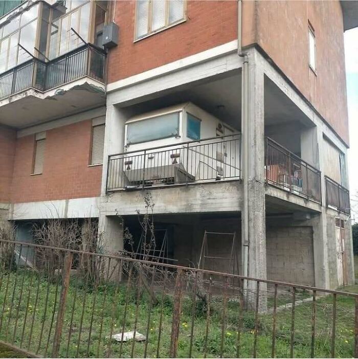 Old caravan awkwardly placed on a concrete balcony of a residential building in Eastern Europe setting.