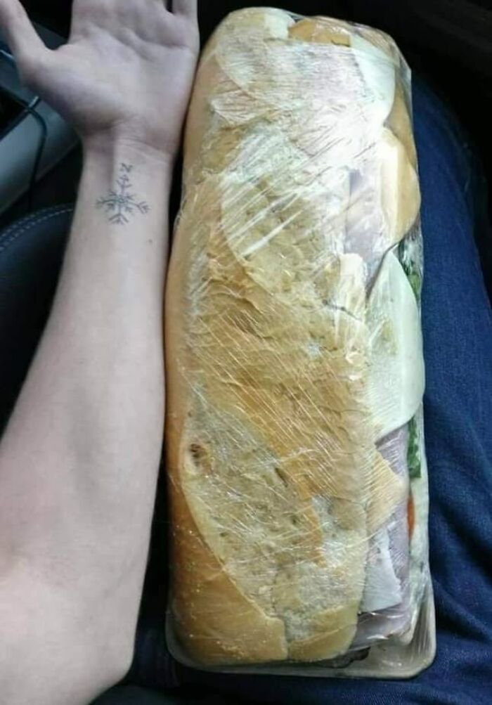 Large sandwich wrapped in plastic on a person's lap, highlighting oversized food humor from Eastern Europe memes.