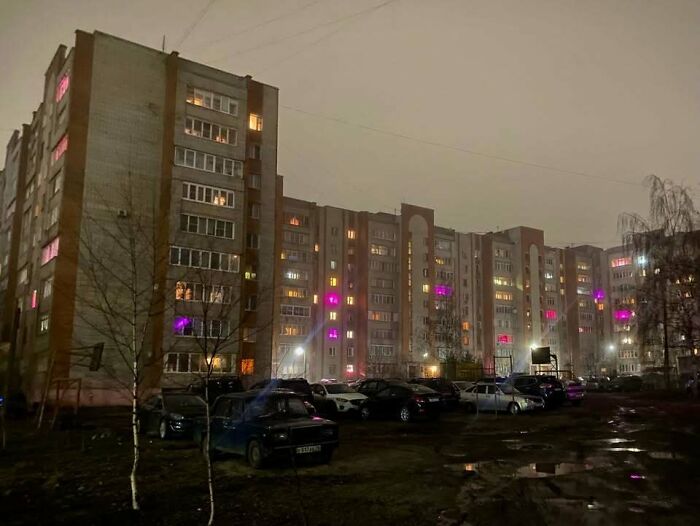 Eastern Europe apartment block at night with colorful lights and parked cars, typical urban residential scene.