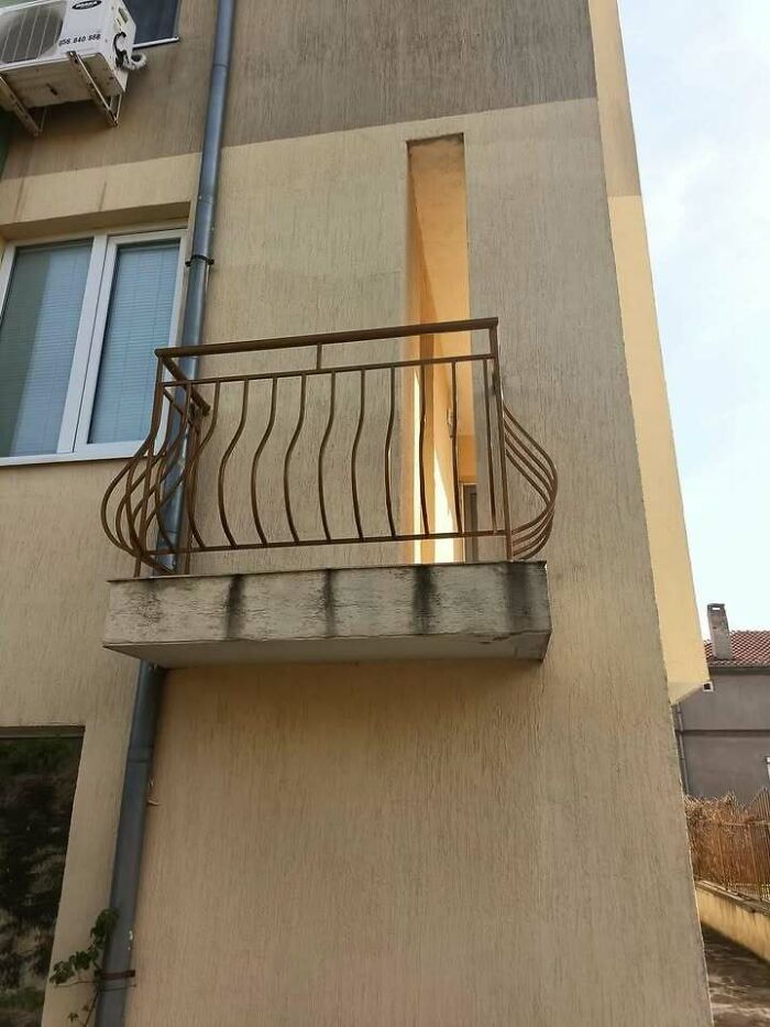 Rusty metal balcony on concrete base with no door access on beige Eastern European apartment building facade.