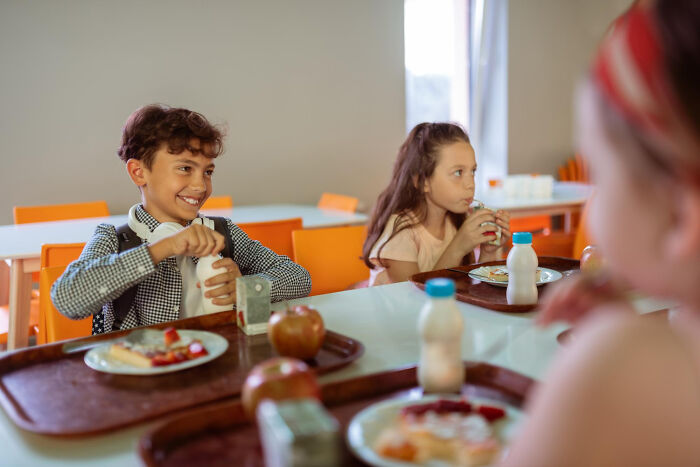 Three kids in a school cafeteria eating lunch and sharing strange and specific kid insults as a unique art form.