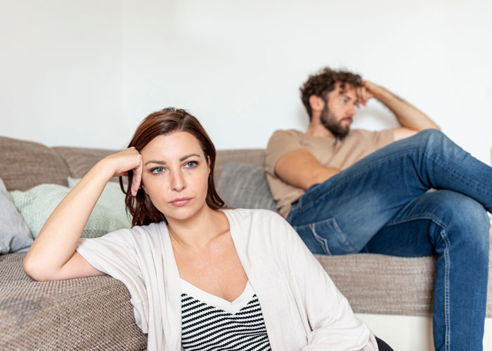 Couple sitting apart on couch looking upset, depicting tough things couples chose to forgive and relationship challenges.