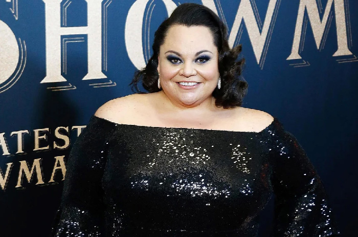 Keala Settle with rare condition smiling and wearing a black sequin off-shoulder dress at an event backdrop.