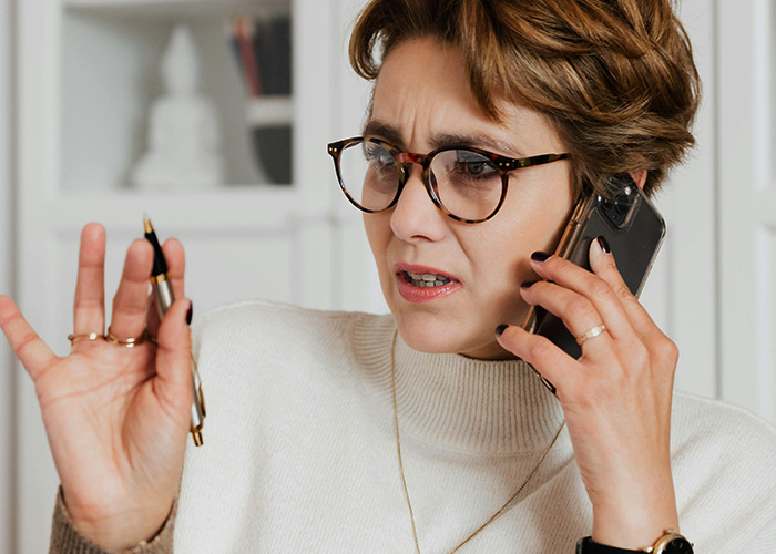 Woman wearing glasses looking confused while talking on phone, illustrating 911 operators handling non-emergency calls.