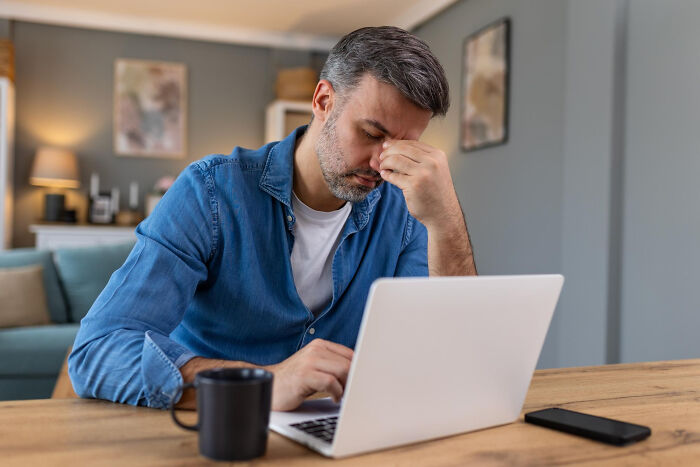 Man sitting at a desk with a laptop, looking stressed and overwhelmed by unexpected family drama.
