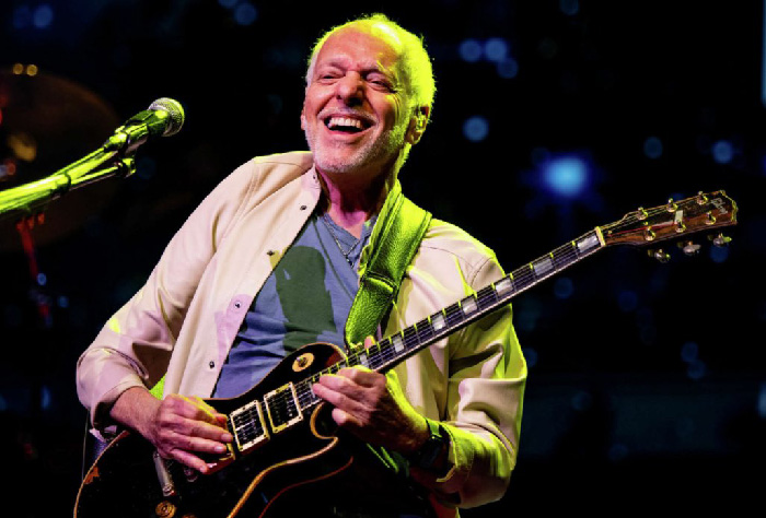 Peter Frampton smiling while playing electric guitar on stage, representing celebrities with rare conditions reality.
