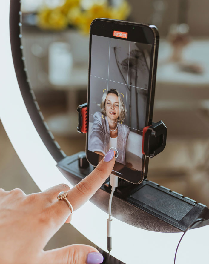 Woman recording video selfie with phone on ring light setup, illustrating things women do to seem attractive men dislike.