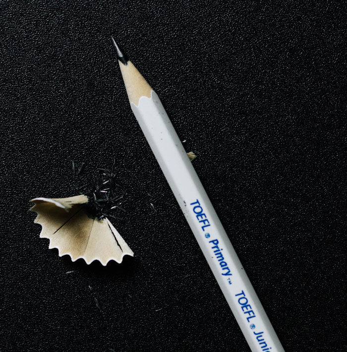 Sharpened white TOEFL pencil with shavings on a black textured surface, symbolizing kids next-level evil concept.