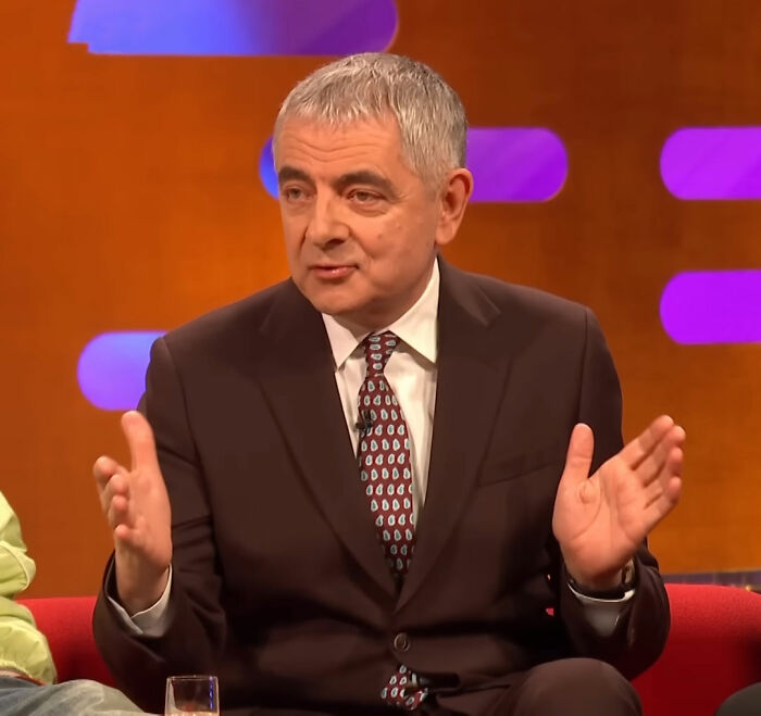 Man in a dark suit speaking with hand gestures on a brightly lit talk show set about Timothée Chalamet Love Actually misread. Man in a dark suit speaking with hand gestures on a brightly lit talk show set about Timothée Chalamet Love Actually misread.