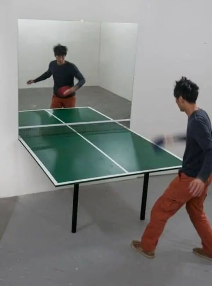 Man playing table tennis against a mirror creating a trippy picture that seems plucked from another reality.