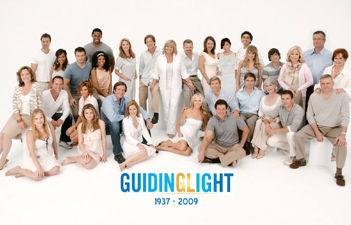 Cast of Guiding Light posing together in a studio, representing one of the longest running TV shows of all time.