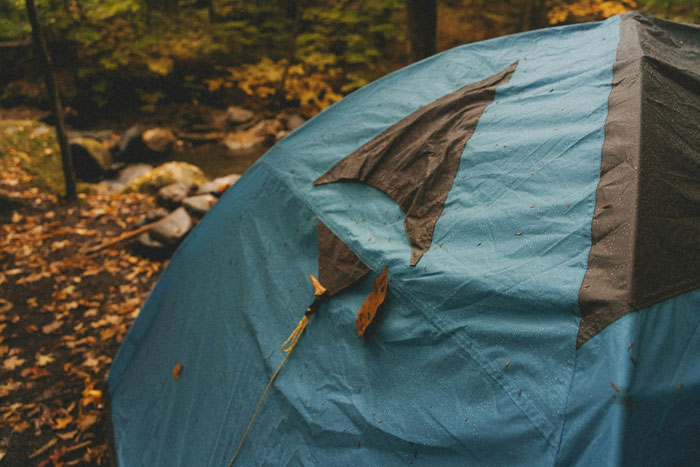 Blue camping tent in the woods surrounded by fallen autumn leaves, evoking a restless outdoor experience.