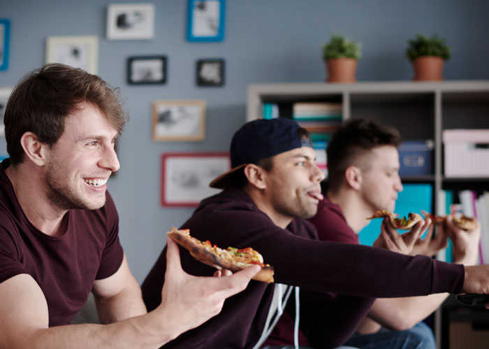 Three young men eating pizza and hanging out at home during a boys’ night, enjoying casual time together. Three young men eating pizza and hanging out at home during a boys’ night, enjoying casual time together.