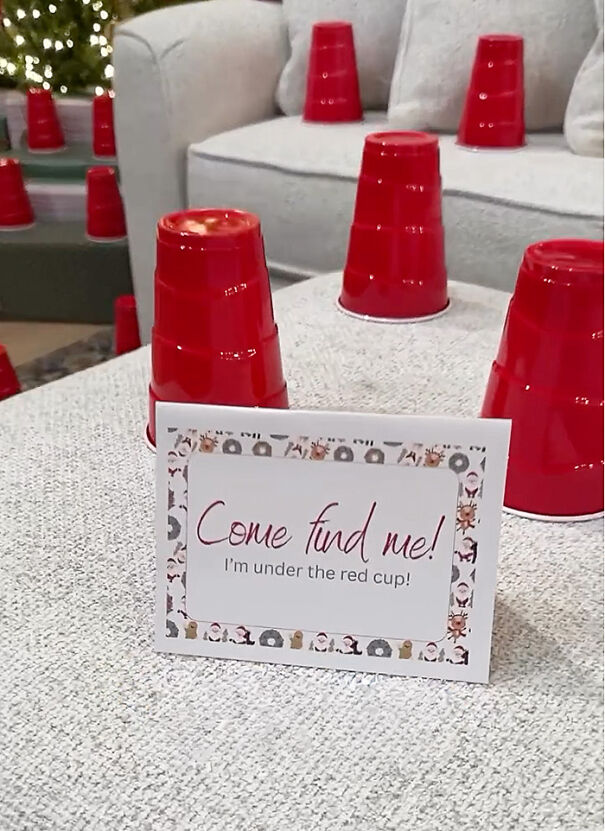 Red cups placed upside down on furniture with a sign indicating an Elf on the Shelf hiding under a cup for a fun scavenger hunt.