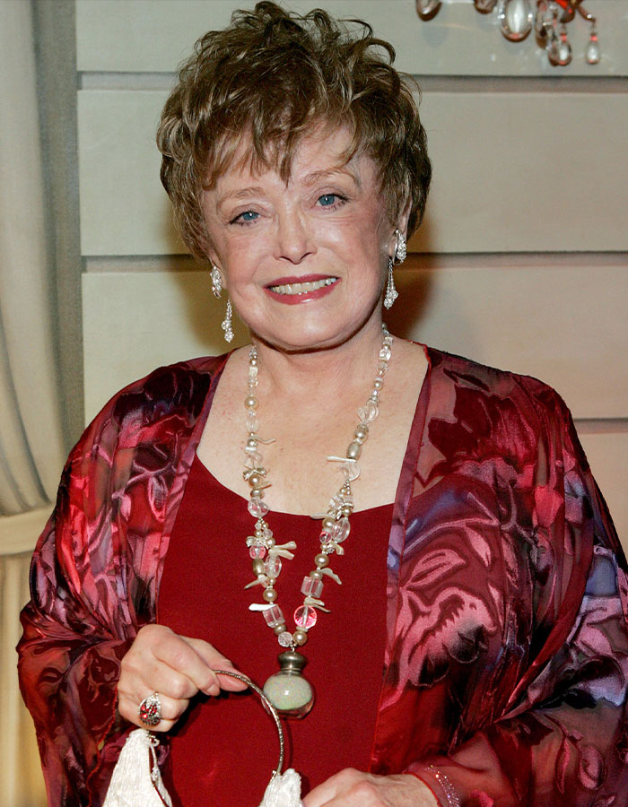 Elderly woman in a red outfit and statement necklace, representing outrageous demands actors put in contracts.