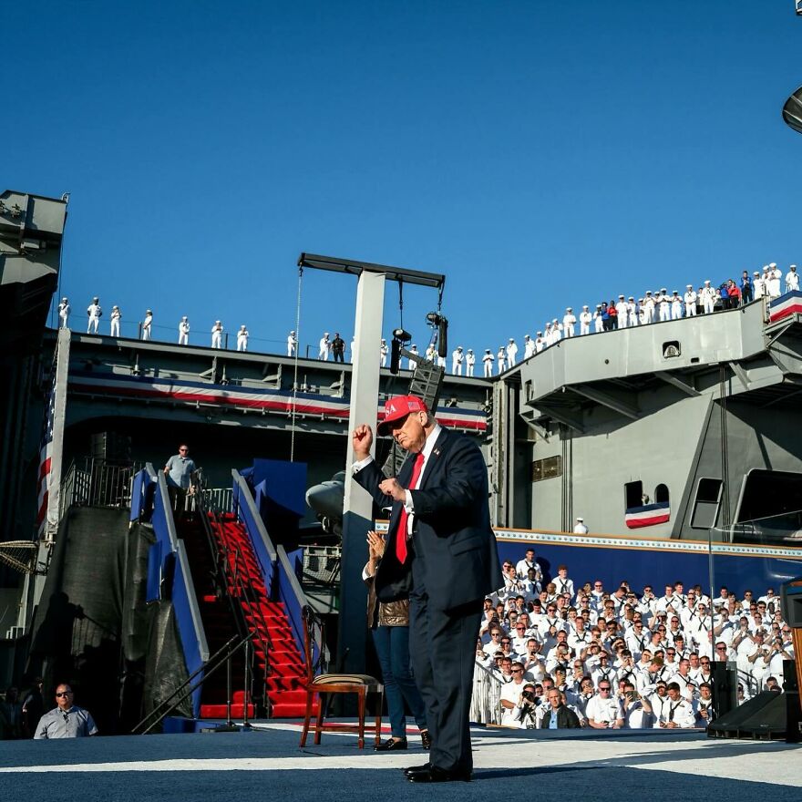 Man in a red hat speaking to a crowd on a ship deck during one of the most unforgettable 2025 pop culture moments.