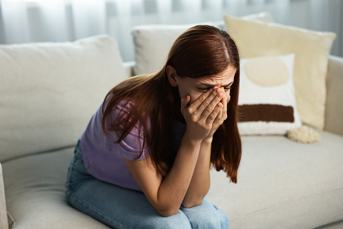 Woman sitting on couch with head in hands upset after family intervention over obsession with brother. Woman sitting on couch with head in hands upset after family intervention over obsession with brother.