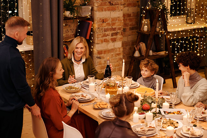 Family gathered around a festive dinner table, with step-grandma watching the baby during babysitting time near holiday lights. Family gathered around a festive dinner table, with step-grandma watching the baby during babysitting time near holiday lights.