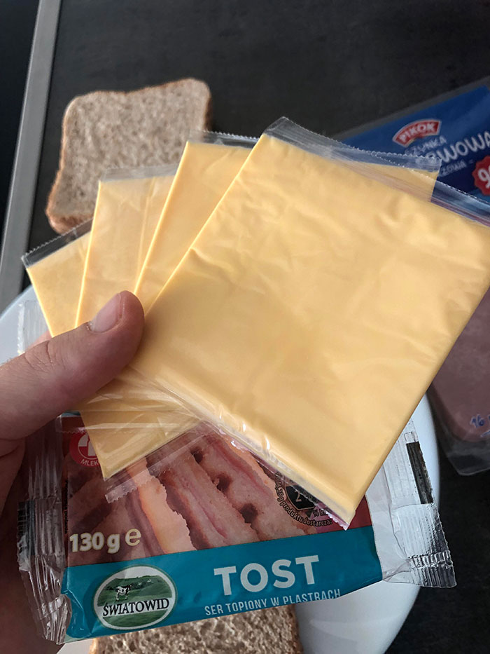 Hand holding multiple slices of processed cheese with sandwich bread in the background for McDonald’s drive thru story.