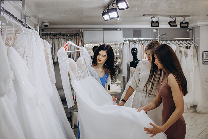 Three women examining a wedding dress during a wedding dress shopping trip signaling a painful friendship wake-up call.