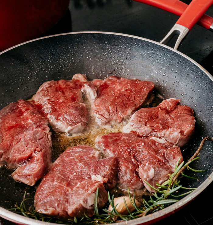 Raw steaks cooking in a pan with herbs and garlic, illustrating a picky eater dealing with allergies situation.