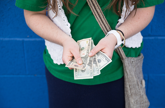 Teen holding cash in hands, standing against a blue wall, illustrating concerns about missing $30k and vague mom answers. Teen holding cash in hands, standing against a blue wall, illustrating concerns about missing $30k and vague mom answers.