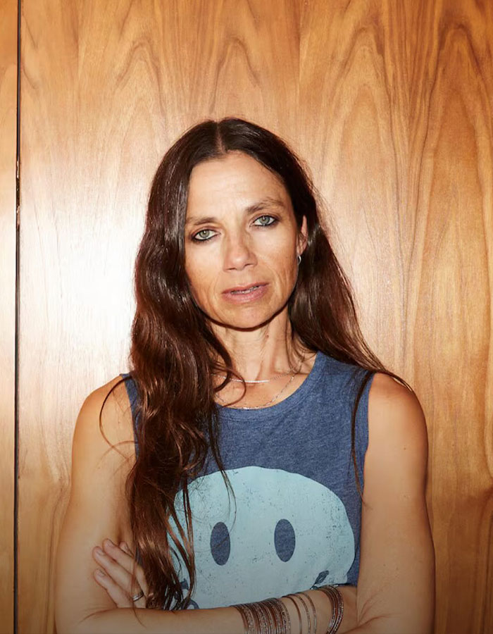 Actress Justine Bateman posing with long hair and arms crossed against a wooden background in casual clothing. Actress Justine Bateman posing with long hair and arms crossed against a wooden background in casual clothing.