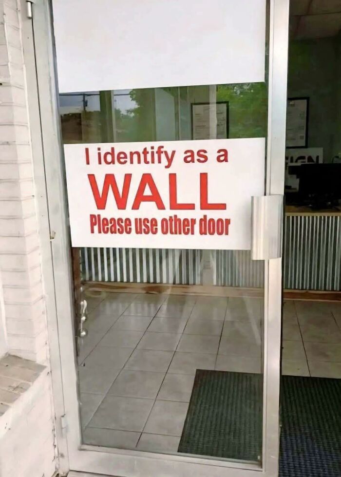 Funny meme on a glass door with red text saying I identify as a wall, asking to use the other door.