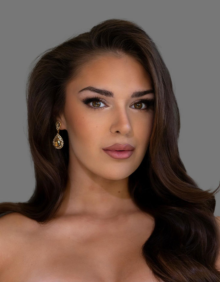 Miss Finland with long brown hair and earrings posing against a gray background in a beauty portrait. Miss Finland with long brown hair and earrings posing against a gray background in a beauty portrait.