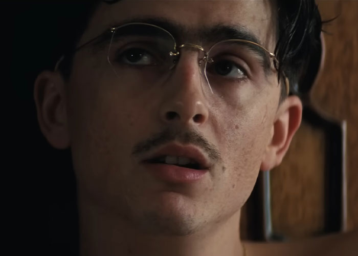 Close-up of Timoth&eacute;e Chalamet wearing glasses, looking thoughtful during an interview amid arrogance criticism online.
