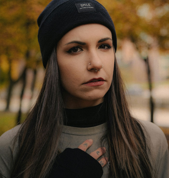Young woman with nose piercings and beanie outdoors, expressing emotions related to things women do to seem attractive men dislike