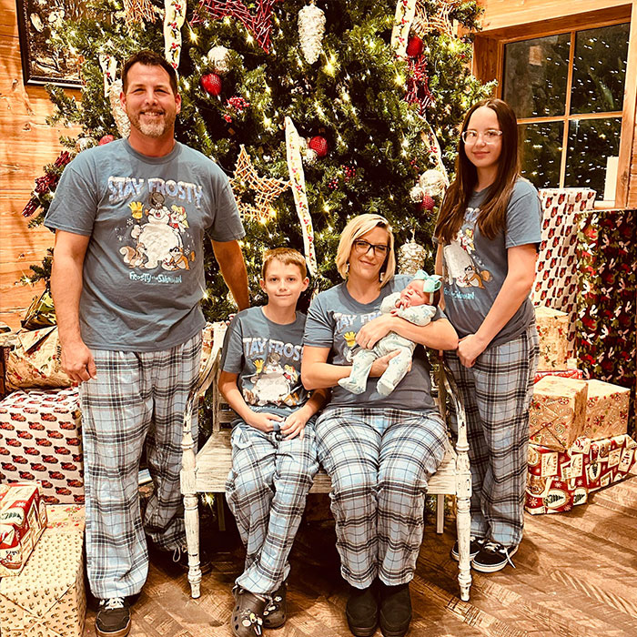 Family dressed in matching pajamas posing by a decorated Christmas tree during a heated NFL argument moment.