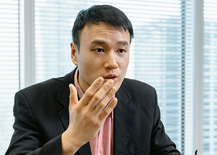 Man taking a call in Korean, wearing a black suit, engaged in a serious conversation in an office setting.