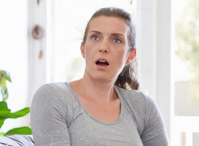 Woman in gray shirt looking shocked and contemplative while deciding to destroy their embryos after a friend's actions revealed.