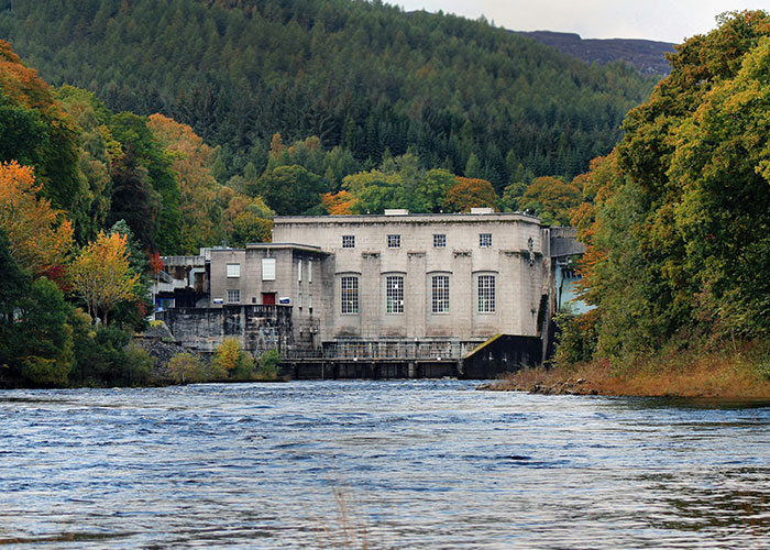 Remote isolated building by river surrounded by dense forest and hills, reflecting creepy and mysterious places witnessed by people.