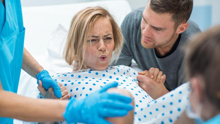 Man looks worried holding partner's hand as she experiences labor pains during delivery with medical staff assisting in hospital room.