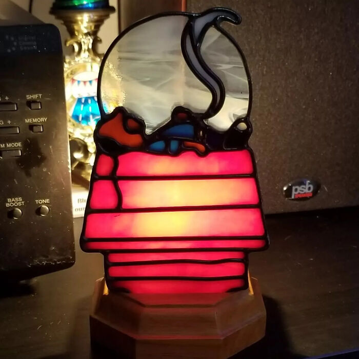 Vivid stained glass sign of Snoopy on his doghouse, showcasing pop culture icon art with bright red and white colors.